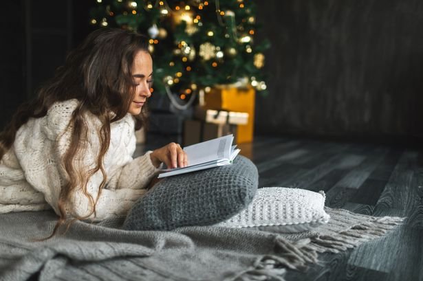 0_Beautiful-woman-reading-book-while-relaxing-on-cushions-by-Christmas-tree-at-home.jpg